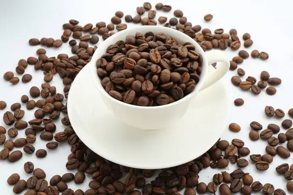 Beyaz arka planda kahve çekirdekleri ve fincanlar, yakın plan.