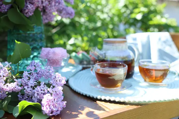Bahçedeki ahşap masada güzel leylak çiçekleri, tatlılar ve çay, yakın plan.