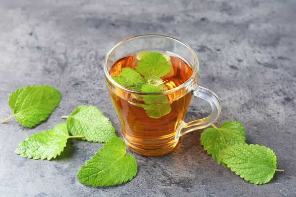 Cam bardakta Aromatik limon merhemi çayı ve gri desenli masada taze yapraklar, yakın plan.
