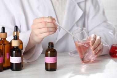 Laboratuvarda beyaz ahşap masada lüks parfüm üreten profesyonel bir parfümcü.