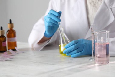 Laboratuvarda beyaz ahşap masada lüks parfüm üreten profesyonel bir parfümcü.