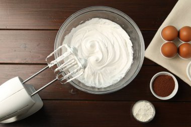Krem şantili kase, el çırpıcısı ve malzemeler ahşap masada, düz yerde.