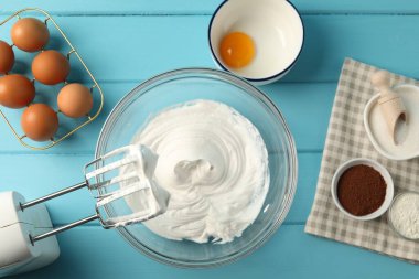 Krem şantili kase, el mikseri ve malzemeler açık mavi ahşap masa, düz yatıyordu.