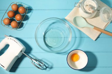 Krem şanti yapıyorum. Kase, el çırpıcı ve malzemeler açık mavi ahşap masada, düz yerde.