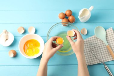 Açık mavi ahşap masada yumurta sarısını beyazdan ayıran kadın.