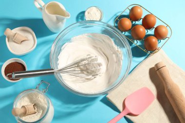 Açık mavi masada çırpılmış krema, yumurta ve diğer ürünlerle çırpın.