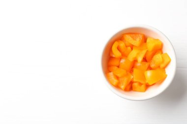 Beyaz ahşap masadaki kasede taze turuncu dolmalık biber parçaları, üst manzara. Metin için boşluk