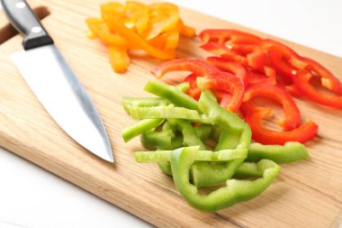 Taze renkli dolmalık biber dilimleri ve beyaz ahşap masada bıçak, yakın plan.