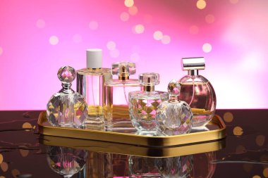 Ayna yüzeyinde birçok farklı parfüm şişesi var. Pembe arka planda bulanık ışıklar, yakın plan.