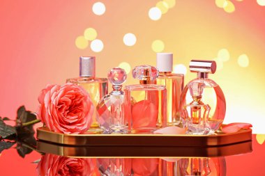 Ayna yüzeyinde çok farklı parfüm şişeleri ve çiçekler mercan zeminine karşı bulanık ışıklarla, yakın çekim