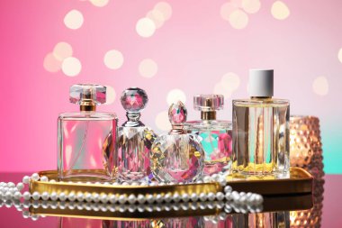 Ayna yüzeyinde birçok farklı parfüm şişesi ve aksesuar var. Pembe arka planda, bulanık ışıklar, yakın plan.