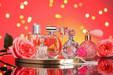 Farklı parfüm şişeleri, aksesuarlar ve çiçekler ayna yüzeyinde kırmızı arka planda bulanık ışıklarla, yakın plan