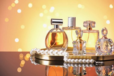 Ayna yüzeyinde turuncu arka planda birçok farklı parfüm şişesi ve aksesuar var.