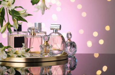 Ayna yüzeyinde birçok farklı parfüm şişesi ve çiçek var. Pembe arka plan, bulanık ışıklar, yakın plan. Metin için boşluk