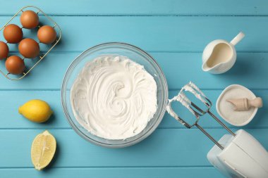 Açık mavi ahşap masa üzerinde çırpılmış krema, yumurta ve diğer ürünlerle el çırpıcı düz yatıyordu.