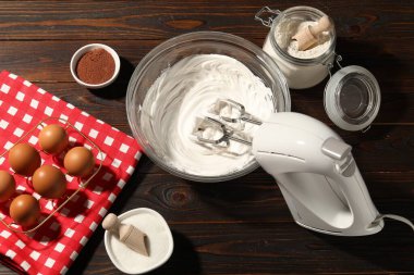 Krem şantili el çırpıcı, yumurta ve diğer ürünler ahşap masada, düz konum