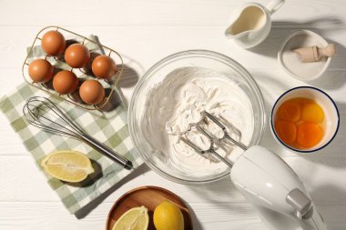 Beyaz ahşap masada çırpılmış krema, yumurta ve diğer ürünlerle el çırpma makinesi.