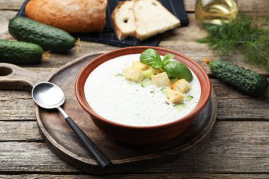 Ahşap masada servis edilen kıtır kıtır salatalık çorbası ve fesleğen.