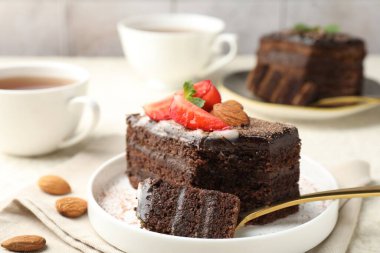 Çilekli, bademli ve masada çay bulunan bir dilim lezzetli çikolatalı pasta.