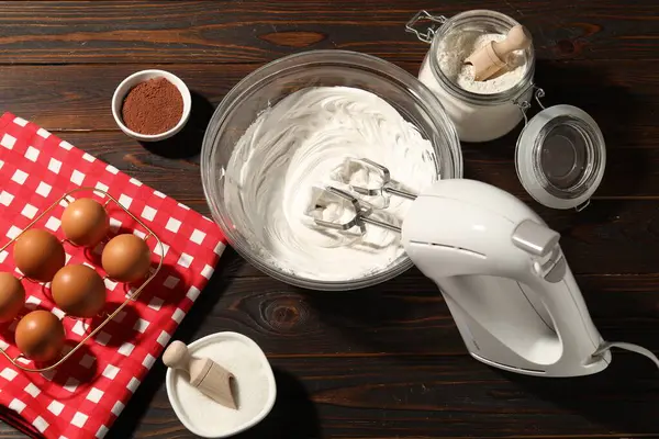 Krem şantili el çırpıcı, yumurta ve diğer ürünler ahşap masada, düz konum