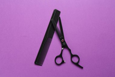 Makas ve tarak menekşe arkaplanda, düz yerde. Kuaför aletleri