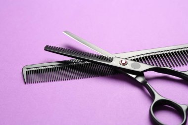 Makas ve tarak menekşe arkaplanda, yakın plan. Kuaför aletleri