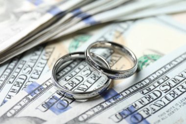 Dolar banknotları üzerinde iki gümüş alyans, yakın plan.