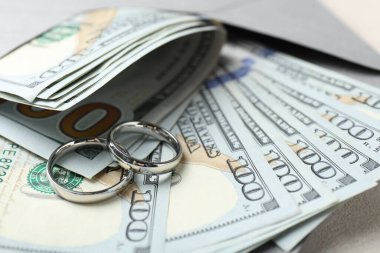 İki gümüş alyans, bir dolarlık banknotlar ve beyaz masanın üzerindeki zarf, yakın plan.