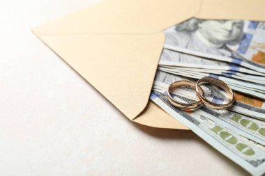 İki altın alyans, bir dolarlık banknotlar ve beyaz masanın üzerindeki zarf, yakın plan. Metin için boşluk