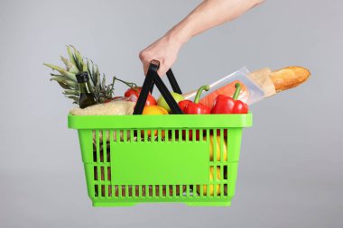 Elinde gri arka planda farklı ürünler olan alışveriş sepeti tutan adam, yakın plan.