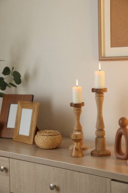 Havalı şamdanlar, yanan mumlar ve kapalı alandaki bej duvarın yanındaki dolaptaki diğer dekorlar.