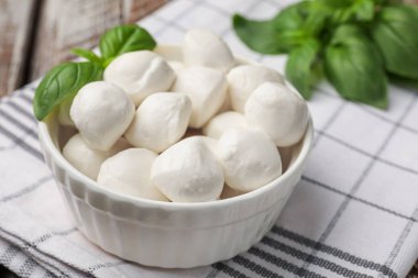 Lezzetli mozzarella peynir topları kasede ve fesleğen masada, yakın plan.