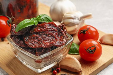 Lezzetli güneşte kurutulmuş domatesler, taze sebzeler, fesleğen ve sarımsak açık gri masada, yakın plan.