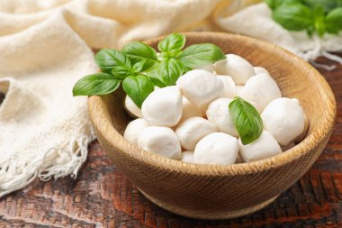 Lezzetli mozzarella peynir topları kasede ve fesleğen ahşap masada, yakın plan.