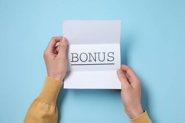 Açık mavi masada elinde kelime bonusuyla kağıt tutan kadın.