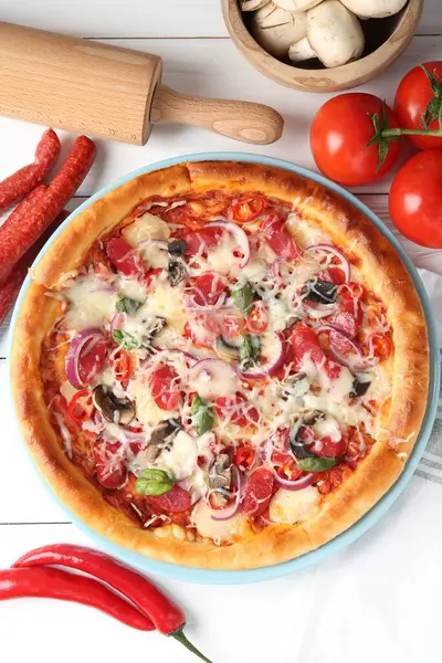 İnce tütsülenmiş sosis ve beyaz ahşap masa üzerindeki malzemelerle nefis bir pizza.