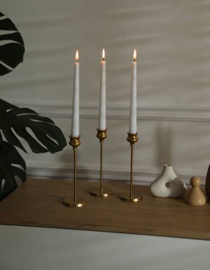 Beyaz duvarın yanındaki çekmecelerin üzerinde yanan mumlar olan şamdanlar.