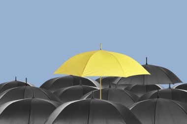 Sarı şemsiye siyah olanlar arasında pastel mavi arka plana karşı