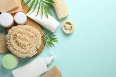 Doğal lif süngerleri, kozmetik ürünleri ve açık mavi arka planda yeşil dallar. Metin için boşluk