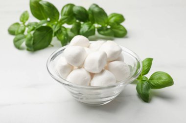 Lezzetli mozzarella peynir topları kasede ve fesleğen beyaz mermer masada, yakın plan.