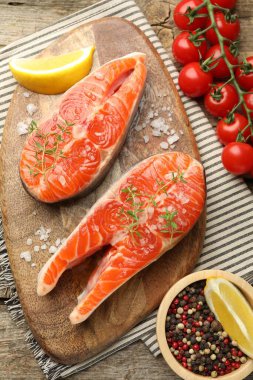 Deniz ürünleri. Somon biftekleri, baharatlar, domatesler ve limon dilimleri masada, düz yerde.
