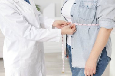 Kilo kaybı. Klinikte kilolu kadının belini bantla ölçen beslenme uzmanı.