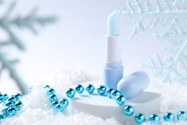 Nemlendirici dudak kremi ve yapay kar üzerine Noel süsü, yakın plan. Kış bakımı