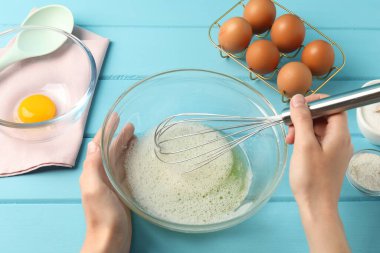 Kadın açık mavi ahşap masada kasede yumurta beyazı çırpıyor.