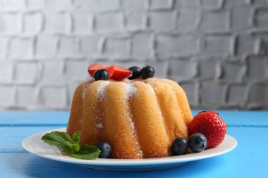 Açık mavi ahşap masada pudra şekerli ve dutlu Lezzetli kek, yakın plan.