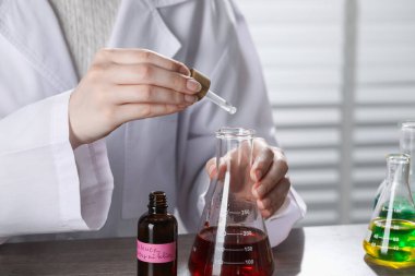 Laboratuardaki ahşap masada lüks parfüm üreten profesyonel parfümcü.