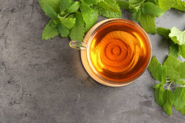 Cam bardakta Aromatik limon merhemi çayı ve gri desenli masa üzerinde taze yapraklar, düz yatak. Metin için boşluk