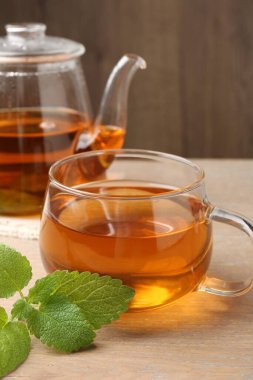 Cam fincanda aromatik limon merhemi çayı, çaydanlık ve ahşap masada taze yapraklar, yakın plan.