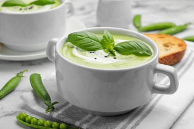 Fesleğenli bezelye kremalı çorba beyaz mermer masada servis edilir, yakın plan.