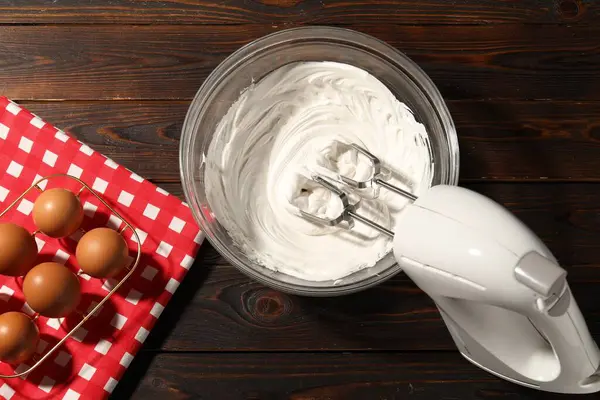 El çırpıcı, kasede krema ve ahşap masada yumurta.